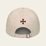 A light beige baseball cap shown from the back, featuring a dark red Iron Cross emblem embroidered in the center and an adjustable strap with a metal buckle at the bottom.