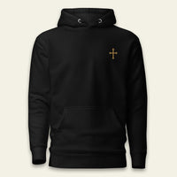 A black pullover hoodie with a small gold cross printed on the left chest, displayed against a light beige background.