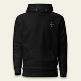 A black pullover hoodie with a small gold cross printed on the left chest, displayed against a light beige background.