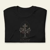 Folded black t-shirt with a cross and vine design on a beige background