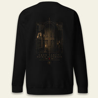 A black crewneck sweatshirt shown from the back, featuring a detailed ST. BENEDICT cross and ON OLD architecture in gold and brown tones, with the text 'CRUX SANCTI PATRIS BENEDEICTI' printed below.